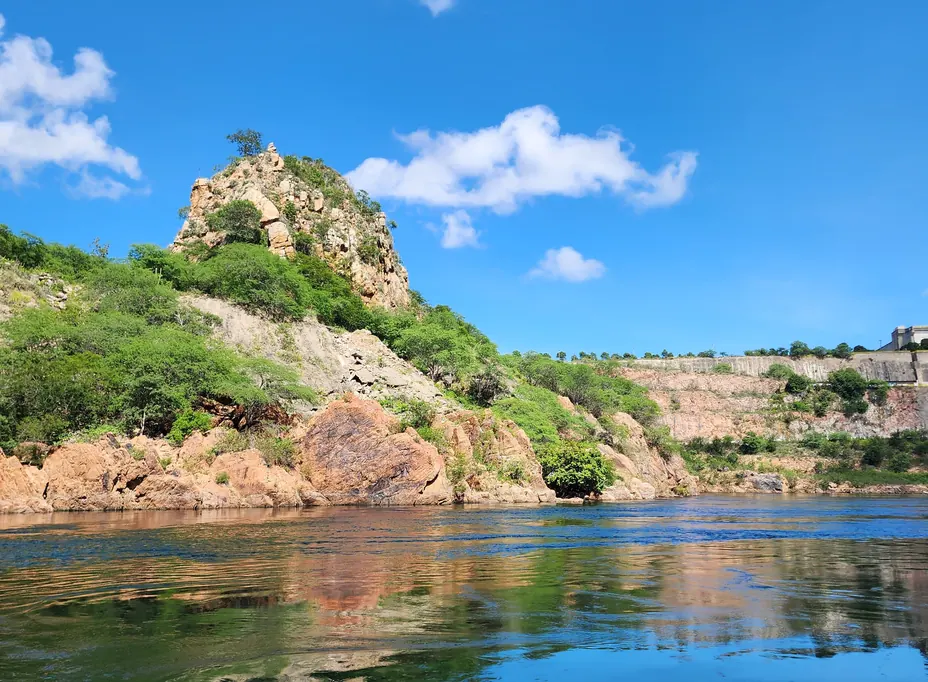 Lago de águas calmas ao pé de um morro rochoso coberto de vegetação da Caatinga, sob céu azul